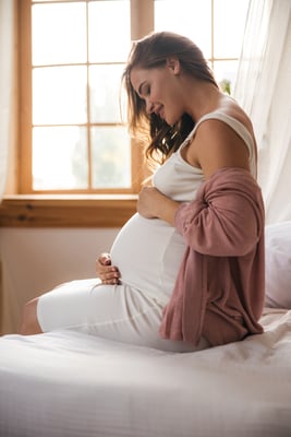 Pregnant Woman Caressing and Smiling her Baby Bump while Sitting on a Bed
